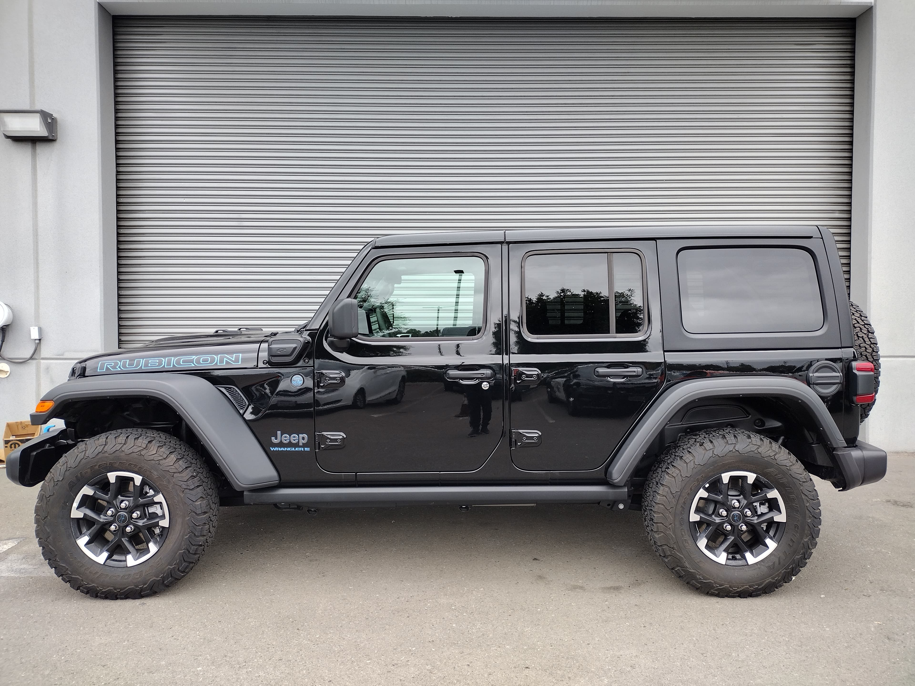 Black Jeep Wrangler Rubicon 4xe side profile parked in front of a grey metal door.